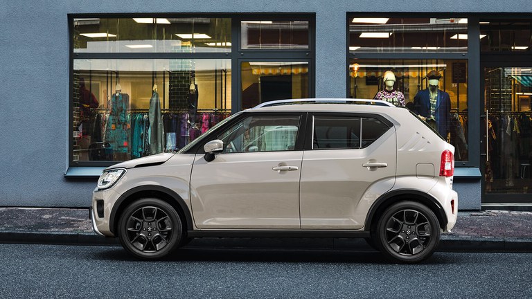 Suzuki Ignis Hybrid in Caravan Ivory Pearl Metallic steht hinter einer Frau im karierten Oberteil.