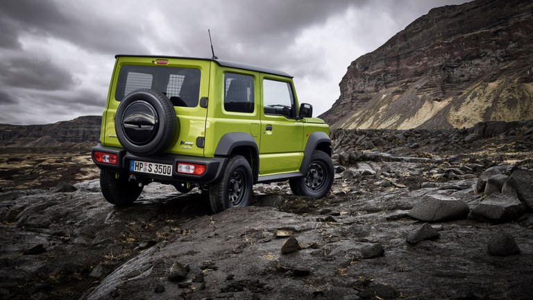 Seitlich von hinten fotografierter Suzuki Jimny Hybrid in Kinetic Yellow, auf Felsen.