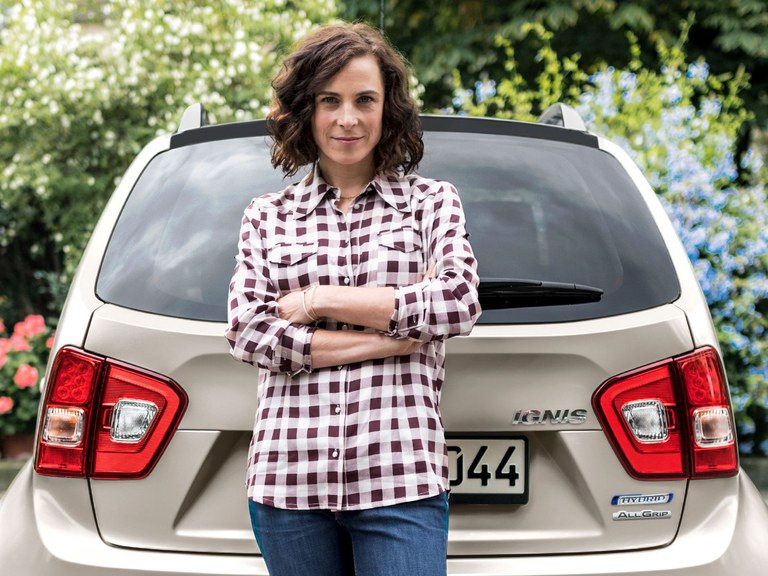 Eine Frau steht vor dem Heck eines Suzuki Ignis Hybrid in Pure White Pearl Metallic.